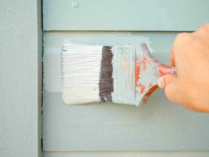 Handen håller pensel målning timmer vägg